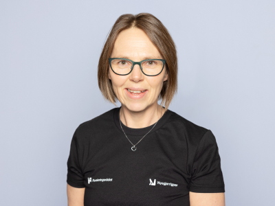 Dame som står foran en grå bakgrunn og smiler til kameraet