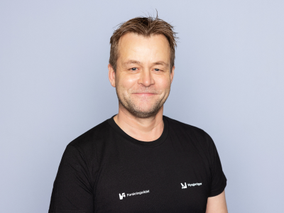 Mann som står foran en grå bakgrunn og smiler til kameraet