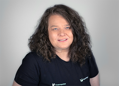 Dame som står foran en grå bakgrunn og smiler til kameraet