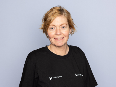 Dame som står foran en grå bakgrunn og smiler til kameraet