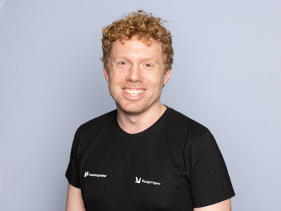 Mann som står foran en grå bakgrunn og smiler til kameraet