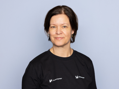 Dame som står foran en grå bakgrunn og smiler til kameraet