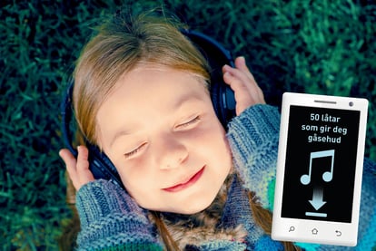 En smilende jente med lukkede øyne og hodetelefoner på ligger i gresset og hører på musikk.