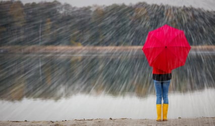 Person med gule støvler som holder en rød paraply i regnvær.