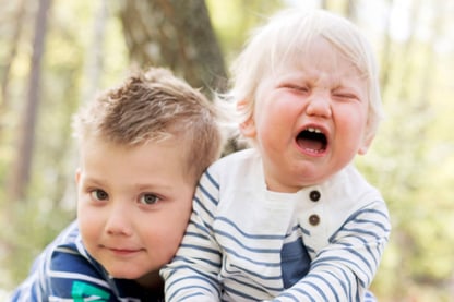 Bilde av en smilende storebror som holder rundt en gråtende lillebror