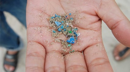 En hånd som holder frem mikroplast i forskjellige farger som er funnet i sanden.