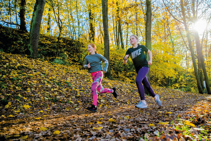 To jenter på løpetur i skogen på høsten.