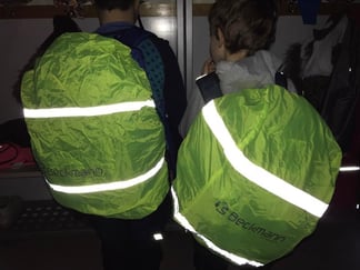 To regntrekk som er trukket over to ryggsekker og med reflekser som lyser i mørket. 