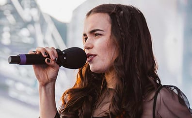 ung kvinne med mørkt hår synger i en mikrofon på en scene