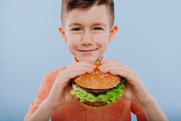 En gutt smiler mens han holder en hamburger klar til å ta en bit. 