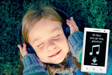 En smilende jente med lukkede øyne og hodetelefoner på ligger i gresset og hører på musikk.