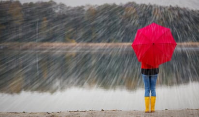 Person med gule støvler som holder en rød paraply i regnvær.