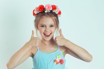 En glad jente smiler og holder begge tomlene opp.