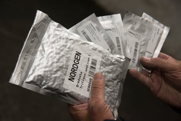 Hender som holder metalliske poser som inneholer frø som lagres i Frøhvelvet på Svalbard