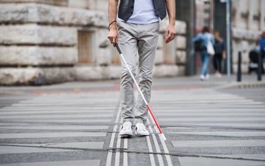 Mann med hvit stokk krysser gaten