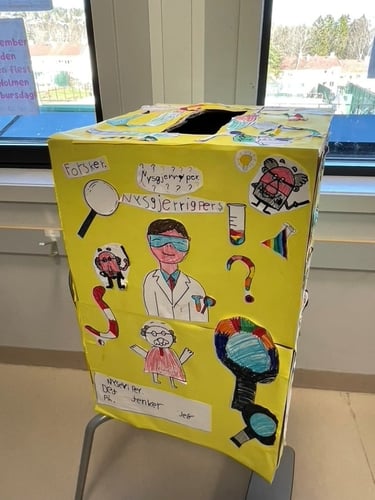 en gul pappboks med tegninger av forskere og forstørrelsesglass og skriften Nysgjerrigper på
