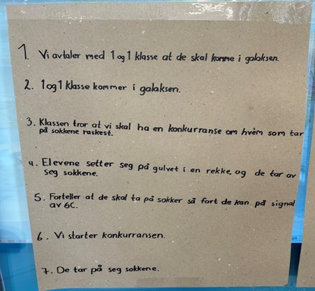 Plakat som ramser opp alle leddene som skal til for undersøkelsen del 1: 1. Vi avtaler med en og en klasse at de skal komme i galaksen. 2, en og en klasse kommer til galaksen 3. klassen tror de skal ha en konkurranse om hvem som tar på sokkene fortest. 4. Elevene setter seg på gulvet i en rekke og de tar av seg sokkene. 5. forteller at de skal ta på seg sokkene så fort de kan på signal av 6c. 6. Vi starter konkurransen 7. De tar på seg sokkene