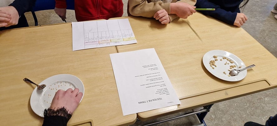 bord med tallerkener med frø på og noen skjemaer elever driver og fyller ut