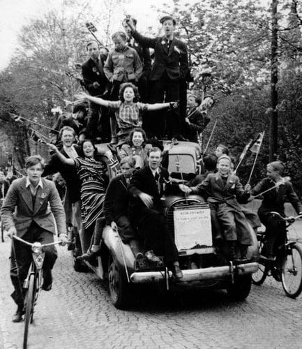 Svart-hvitt bilde av en overfylt bil med glade mennesker med norske flagg