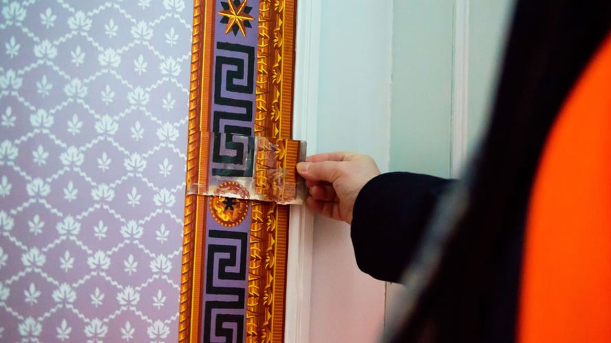 En tapetbit holdes opp mot tapetbord på vegg med samme mønster