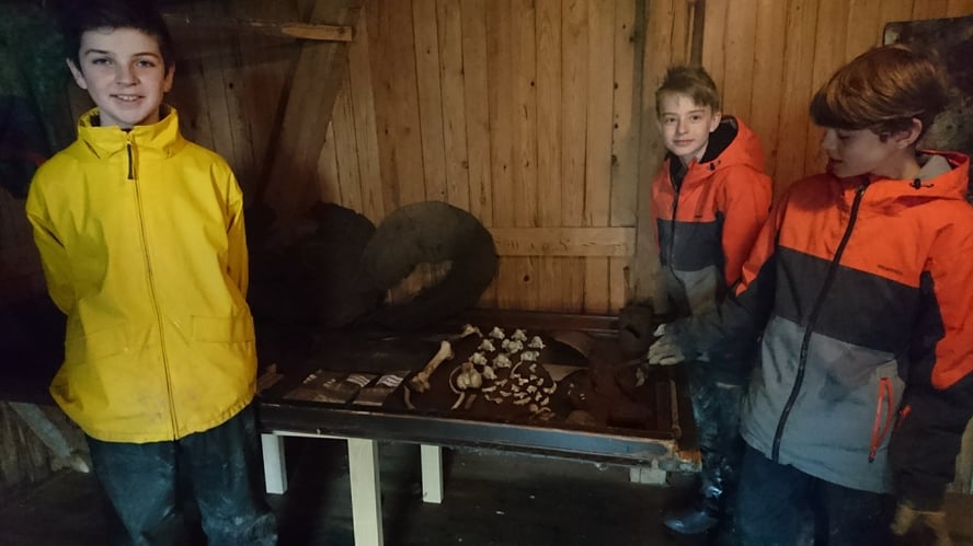 Gutter står foran et bord med metallgjenstander funnet med metalldetektor.