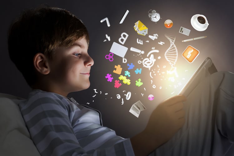 En gutt sitter i mørket og ser på et nettbrett som lyser mot han