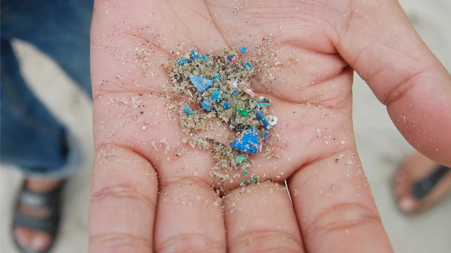 En hånd som holder frem mikroplast i forskjellige farger som er funnet i sanden.