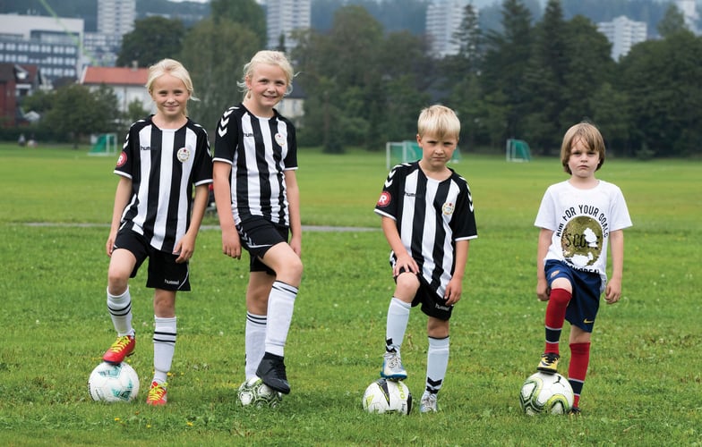 To jenter og to gutter med fotballdrakter og fotballer