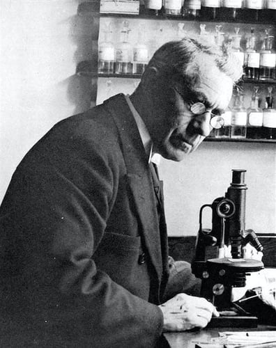 Gammelt svarthvitt foto av mann med mikroskop og små glassflasker i bakgrunnen