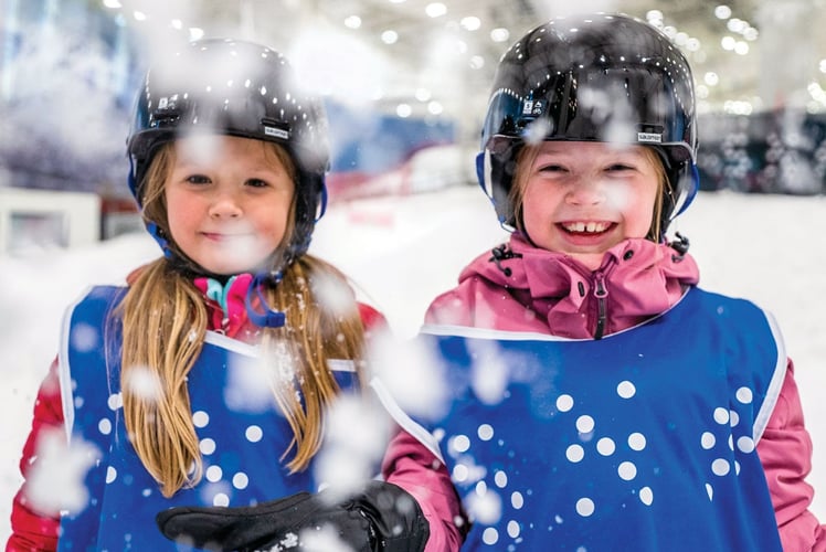 To smilende jenter med hjelm og snøfnugg i lufta rundt