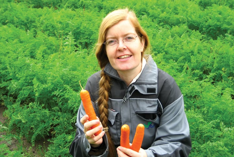 Dame med lyst hår som holder gulerøtter