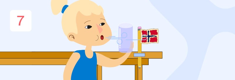 En jente med lyst hår i hestehale som blåser på et glass