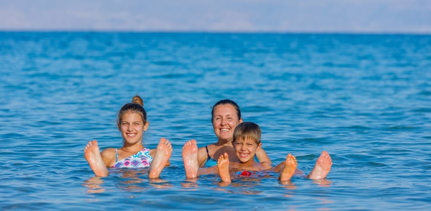 En mor og to barn flyter i dødehavet med bena over vannflaten