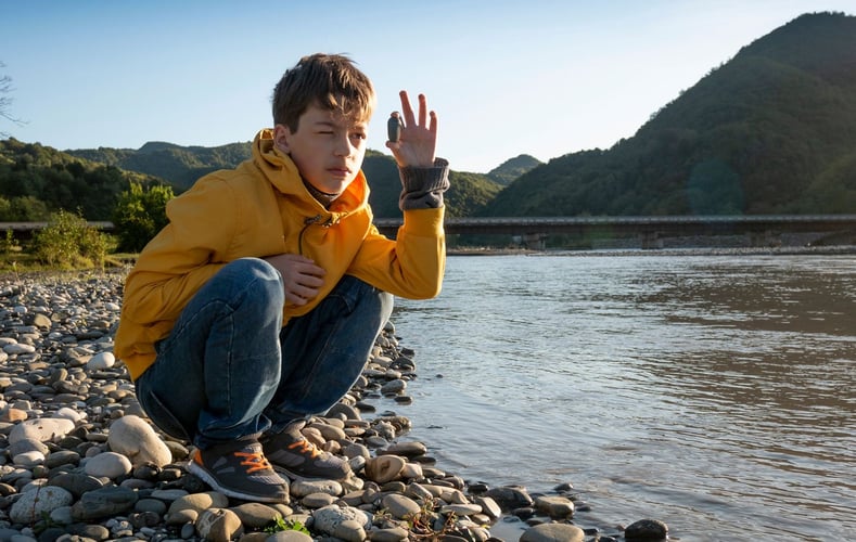 Gutt sitter på strand og studerer stein