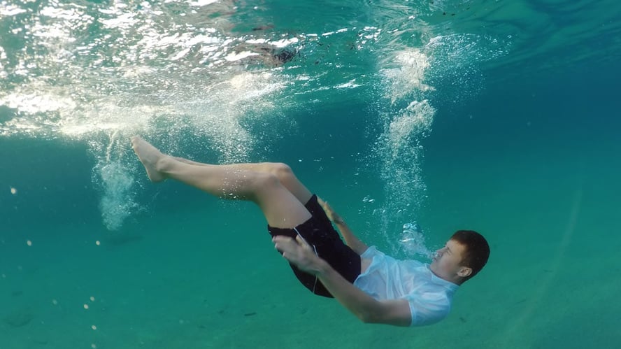 Mann på vei ned i vannet baklengs med klærne på.