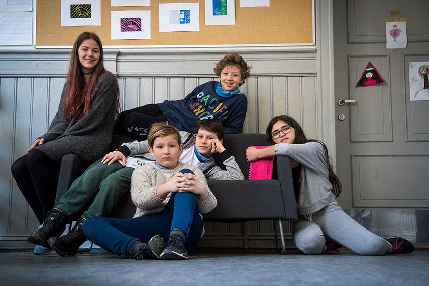 Gruppe barn som sitter eller ligger på en sofa på skolen.