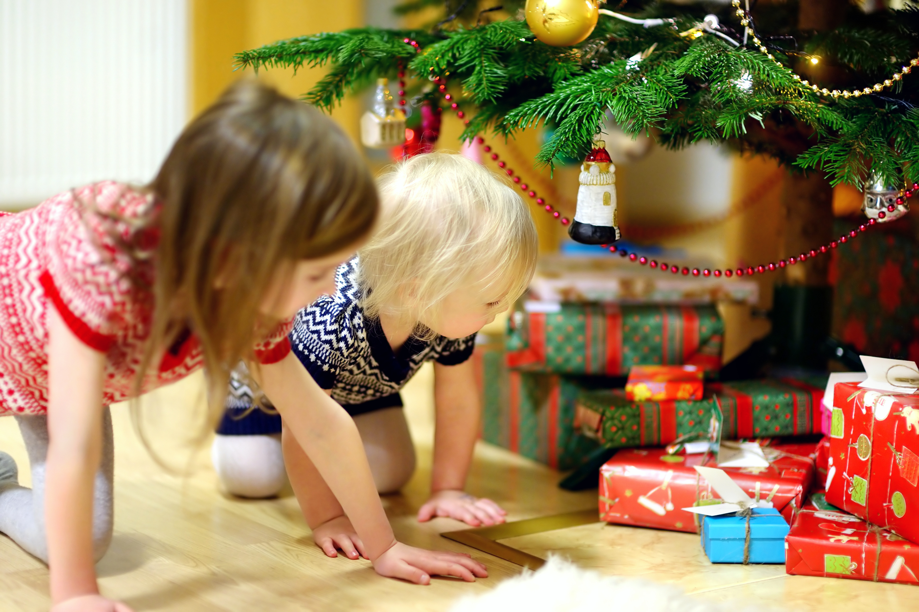 To barn sitter på kne og ser på julegavene som ligger under juletreet.