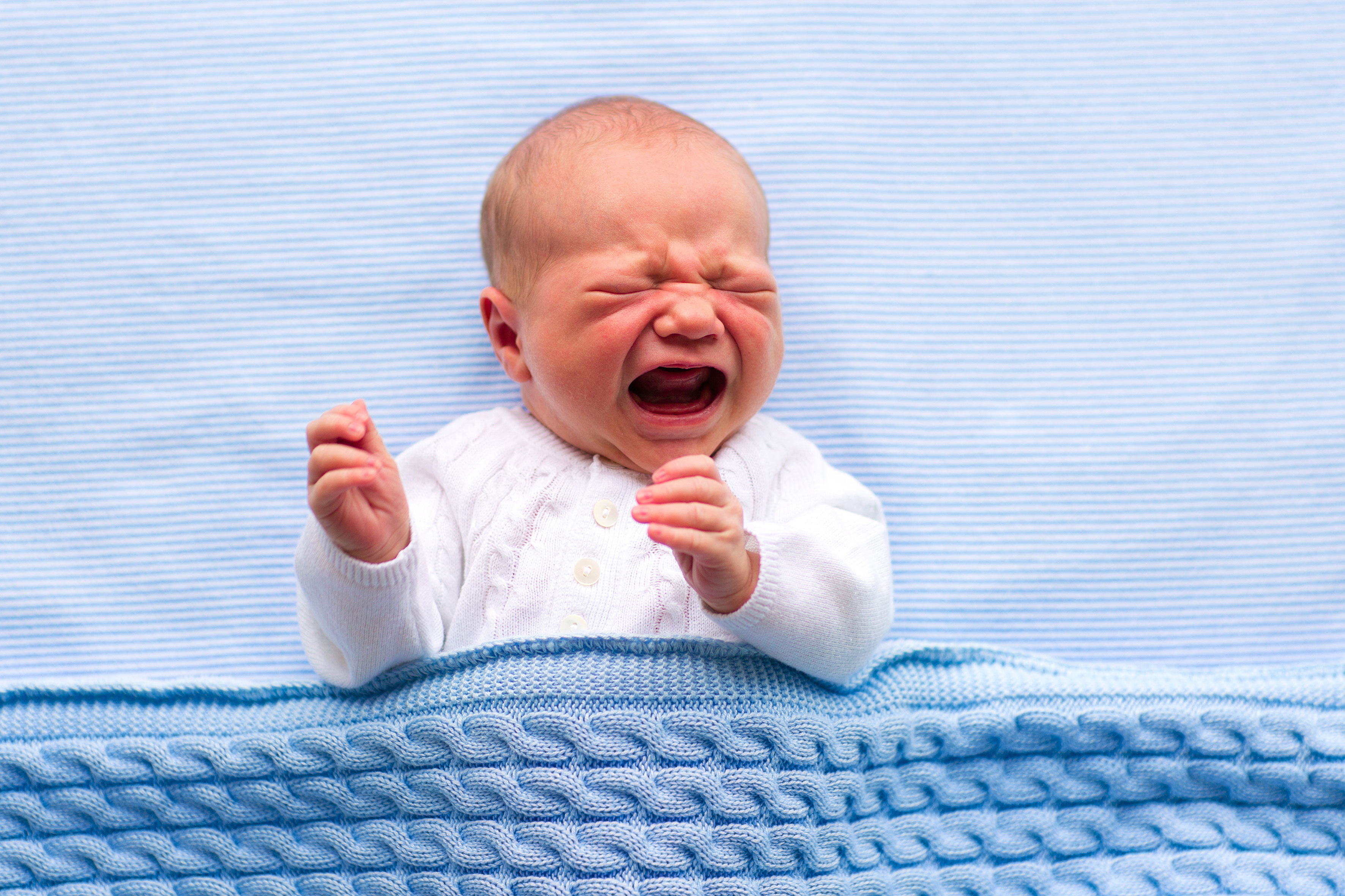 En baby ligger i sengen og gråter