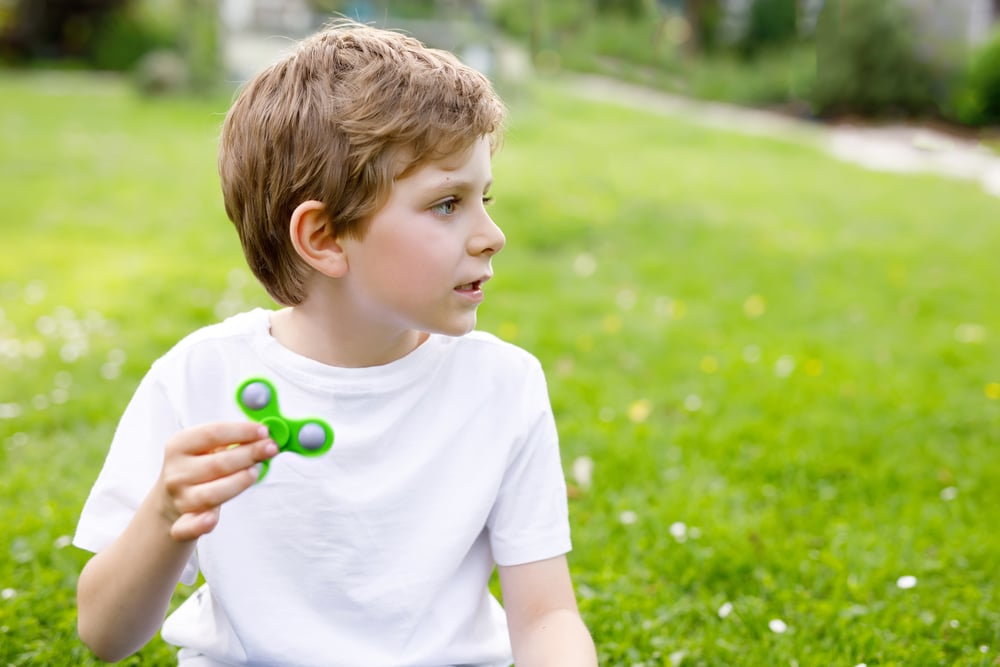 En gutt som sitter i gresset og leker med en fidget spinner.