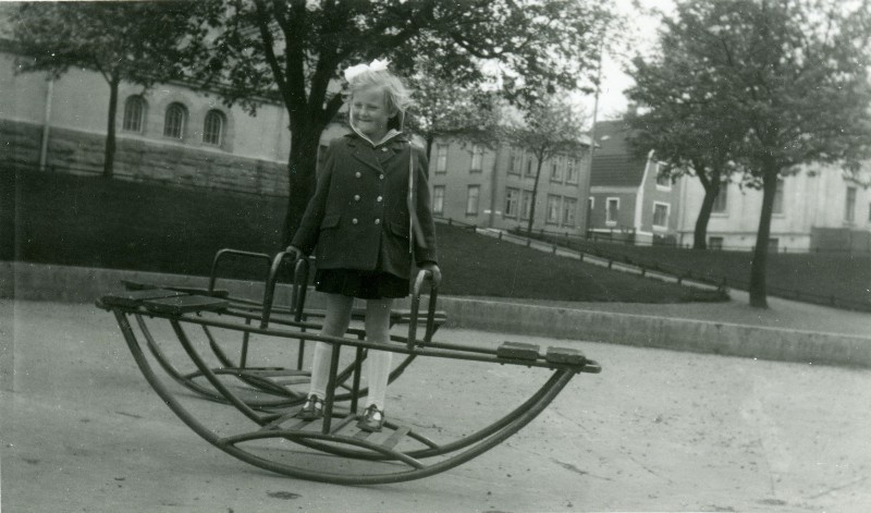 Et sort-hvitt bilde av en jente som leker på en lekeplass i gamle dager.