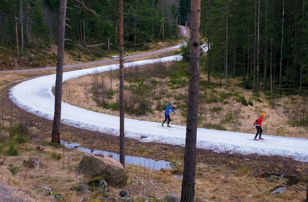 To skiløpere på en trase med kunstig snø i en grønn skog