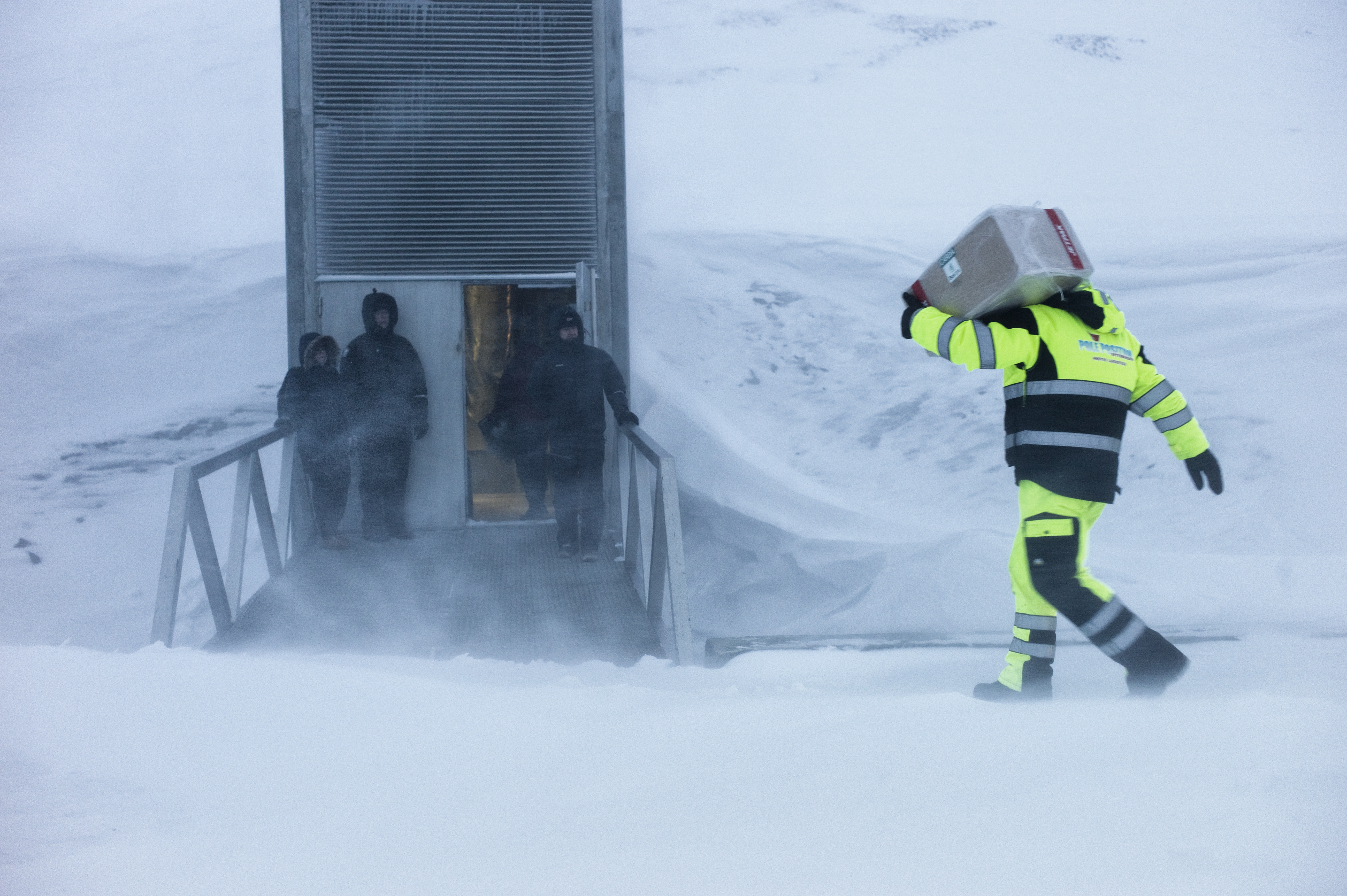 Bilde av Frøhvelvet på Svalbard om vinteren. Tre personer står foran inngangen og en person kommer bærende på en kasse.