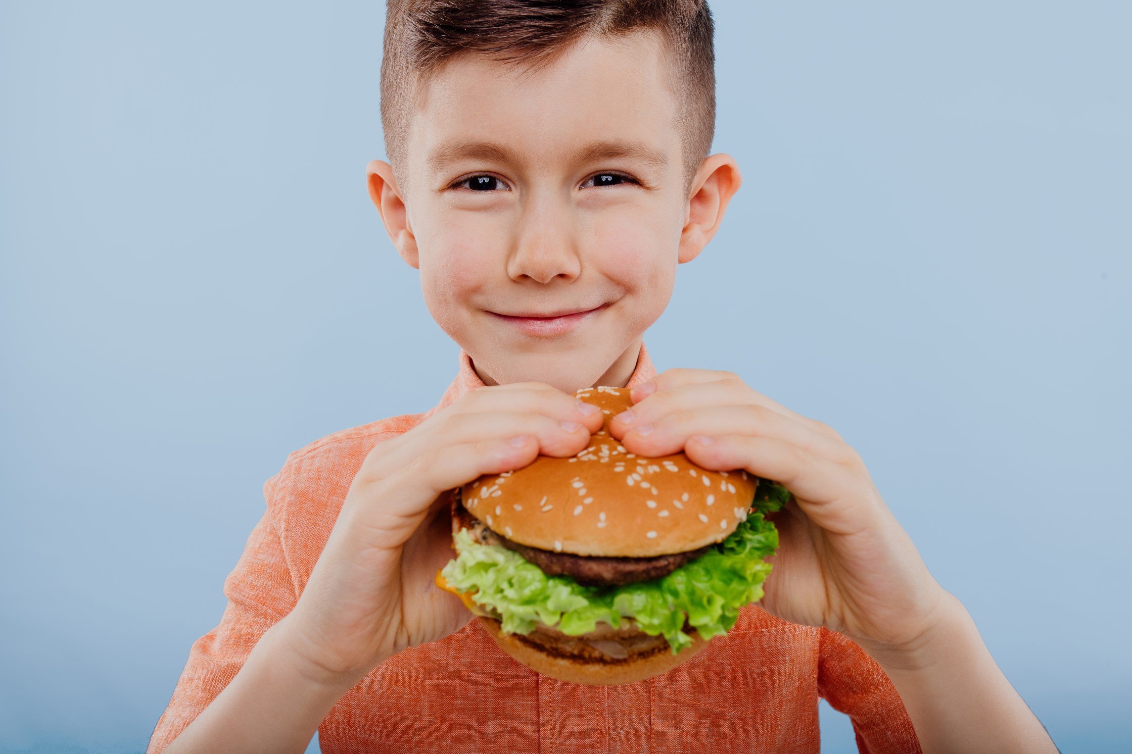 En gutt smiler mens han holder en hamburger klar til å ta en bit.